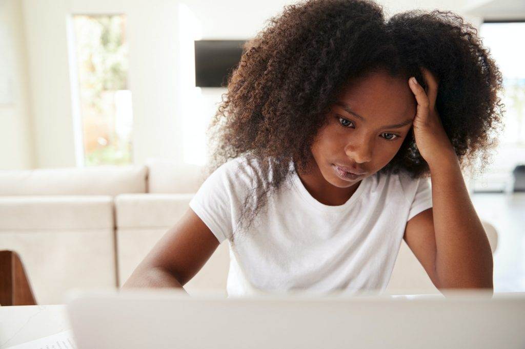 Young teenage black girl using laptop computer at home, close up